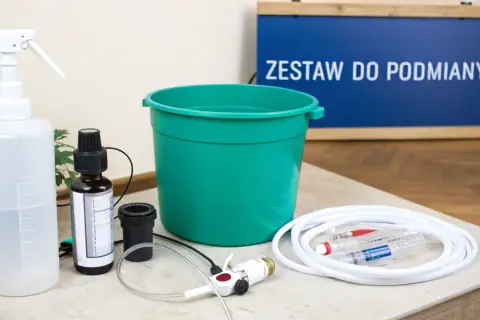 Zestaw do podmiany wody w akwarium: butelka z atomizerem, pojemnik, wężyk, strzykawki i buteleczka z płynem, prawdopodobnie antychlor.